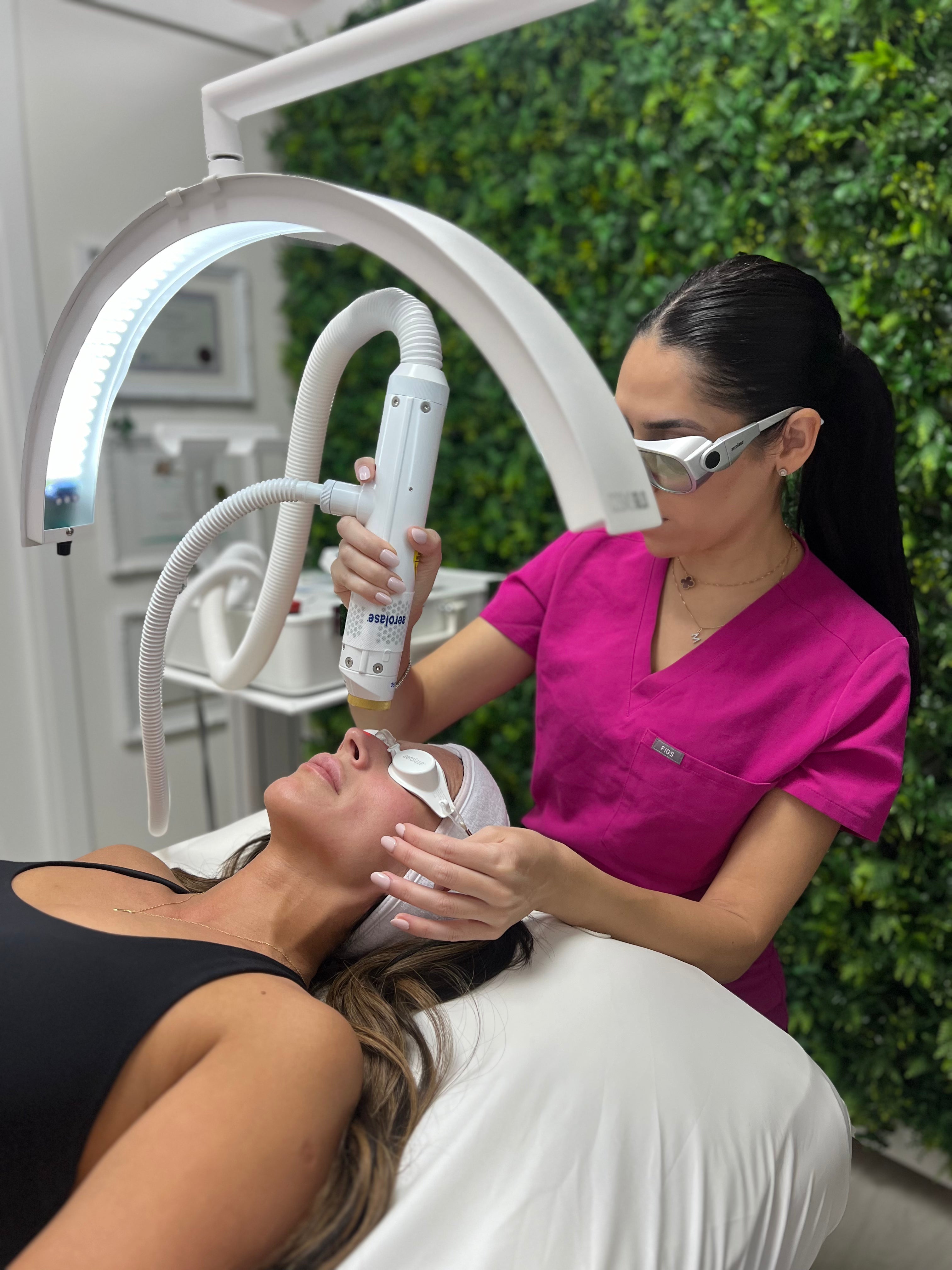 An aesthetician in pink scrubs performing an AEROLASE laser treatment on a woman lying on a treatment bed at My Skin Spot medical spa in Vancouver.