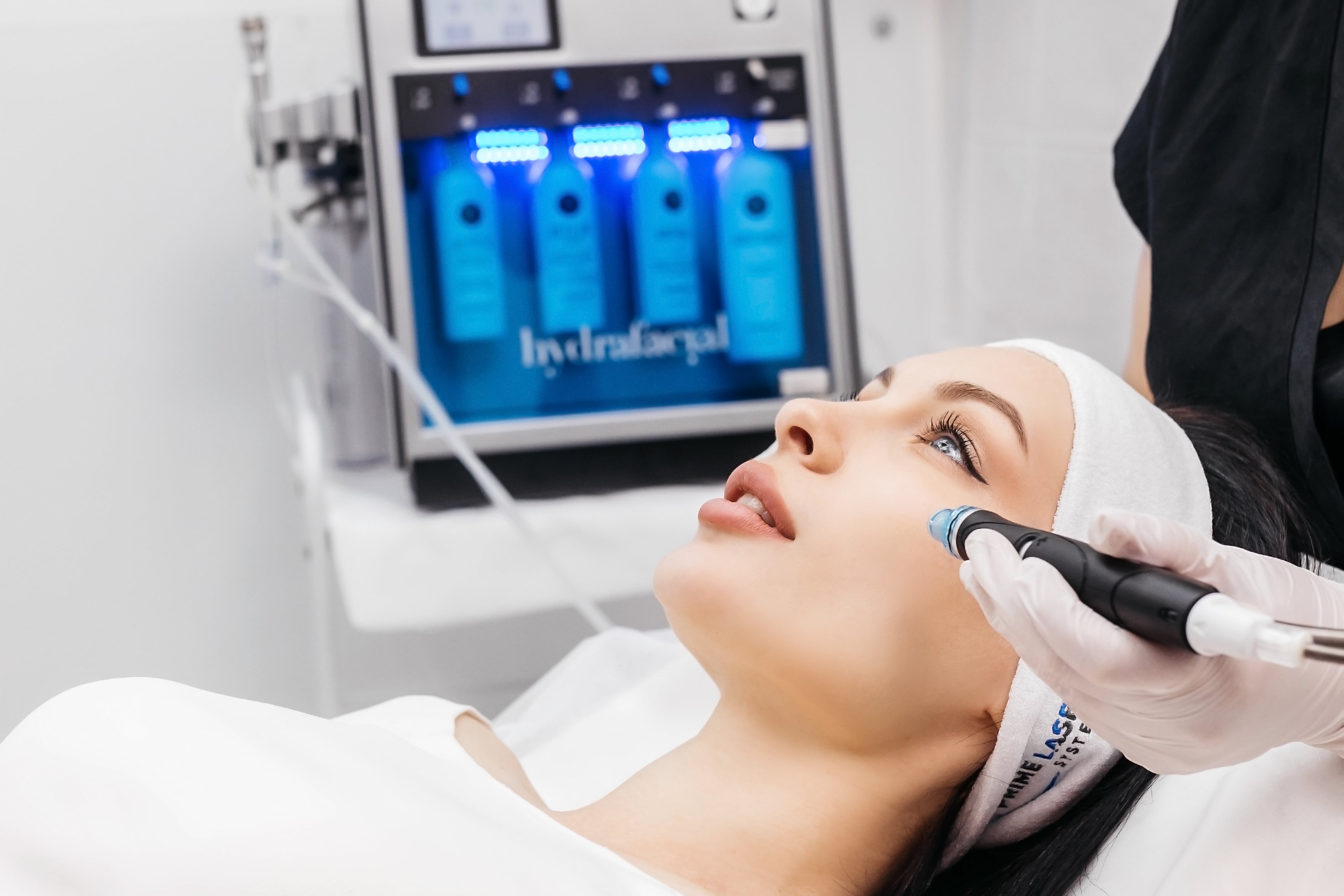 An aesthetician performing a HydraFacial treatment on a woman lying on a treatment bed, with the HydraFacial machine visible in the background at My Skin Spot medical spa in Vancouver.